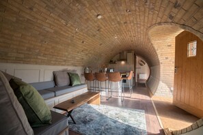 Ein gemütlicher Innenraum mit Ziegeldecke, einer Holztür und einer Sitzecke mit Sofa und Sesseln.