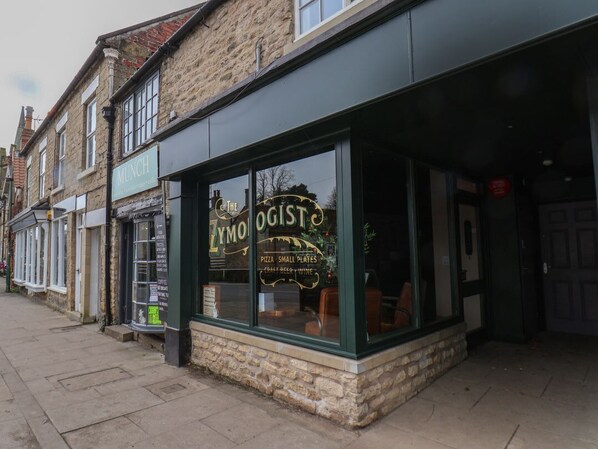 A building with a storefront named 'The Zoologist,' featuring a signboard with the establishment's name and offerings like pizza, small plates, and wine.
