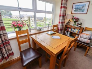 A cozy room with a wooden table, chairs, a bookshelf, a window with a view, and a framed picture on the wall.