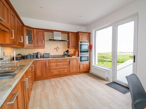Eine moderne Küche mit Holzschränken, einem Einbauofen und einem großen Fenster mit Blick ins Grüne.