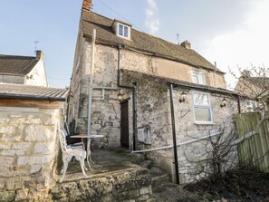A stone building with a small porch, a table, and a chair. - Combe Cottage, Stroud (Stroud)