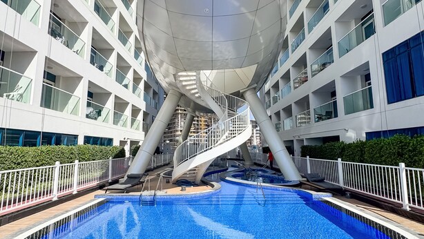 A modern building with a circular atrium, a central pool, and a spiral staircase. - PVH - Opalz By Danube - Studio with Pool (Dubai)