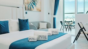A modern hotel room with a bed, a city view, and a dining area. - PVH - Opalz By Danube - Studio with Pool (Dubai)