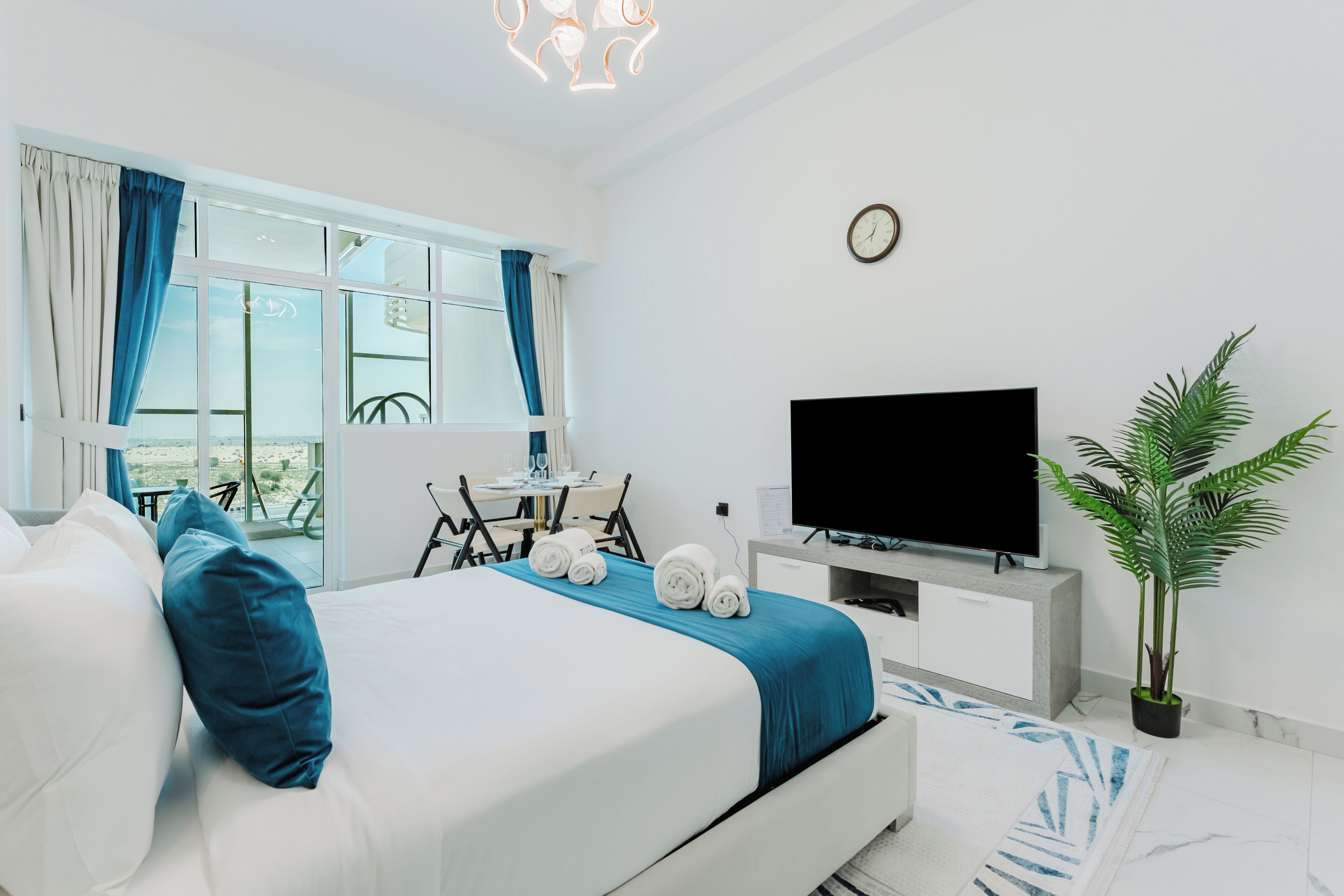 Een moderne hotelkamer met een bed, een flatscreen televisie, een bureau met stoel, een kamerplant en uitzicht op het omliggende landschap.