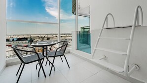 A balcony with a table and chairs, a ladder, and a view of a cityscape. - PVH - Opalz By Danube - Studio with Pool (Dubai)