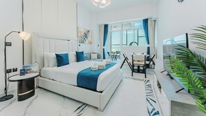 A modern hotel room with a bed, desk, chair, lamp, and a large window. - PVH - Opalz By Danube - Studio with Pool (Dubai)