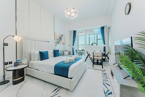A modern hotel room with a bed, desk, chair, lamp, and a large window. - PVH - Opalz By Danube - Studio with Pool (Dubai)