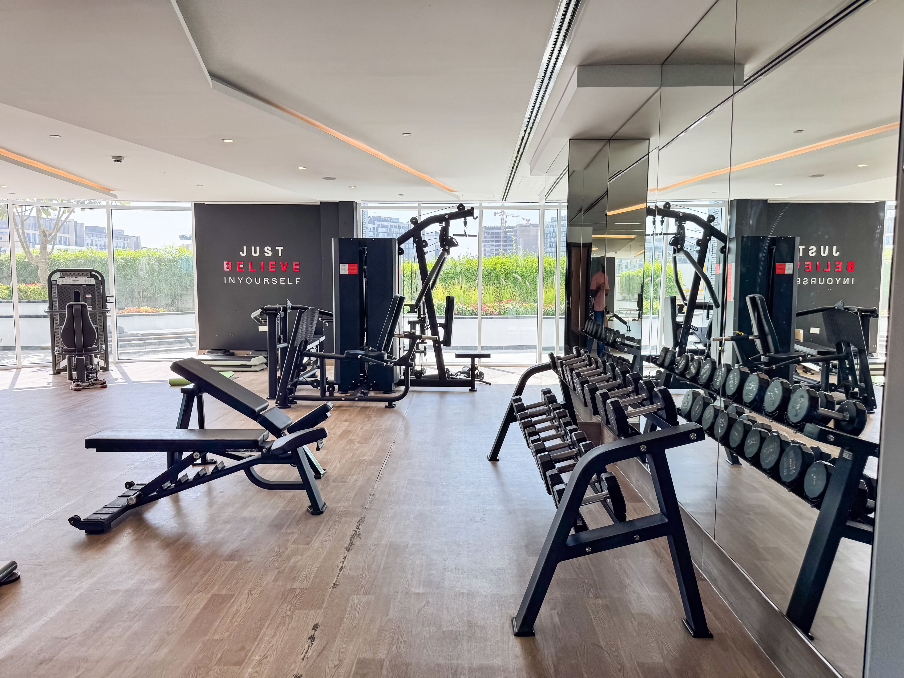 A modern gym with various exercise equipment, large windows, and motivational wall text.