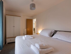 A bedroom with a bed, a wardrobe, a nightstand, and a hanging light fixture. - Rose Cottage, St Ives (St. Ives)