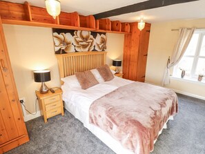 A bedroom with a bed, bedside lamps, a nightstand, a wooden headboard, and a window with curtains.