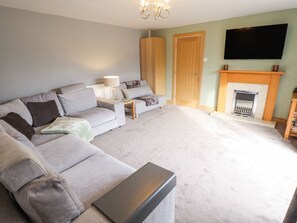 A living room with a sofa, a coffee table, a fireplace, and a television mounted on the wall.