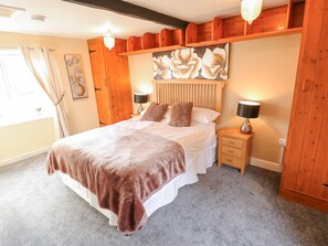 Une chambre à coucher avec un grand lit, une tête de lit en bois, deux lampes de chevet, une table de chevet et une fenêtre avec des rideaux.