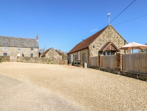A gravel driveway leading to a stone building with a wooden fence and a metal gate. - Stable Cottage, Gatcombe (Newport)