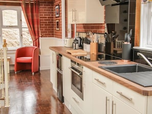 A kitchen with a wooden countertop, a red chair, and a window with curtains. - Ragleth Place Lodge Retreat (Church Stretton)