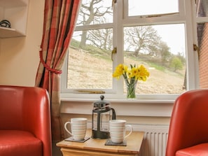 A room with a window, a radiator, a table with a coffee pot and cups, and two red chairs. - Ragleth Place Lodge Retreat (Church Stretton)