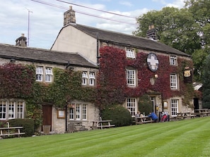 A traditional stone building with ivy-covered walls, a pub sign, and outdoor seating.