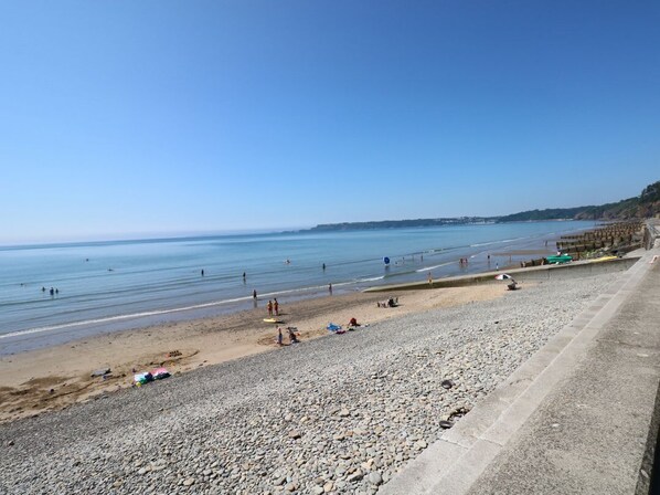 Ein Strand mit Kieselsteinen, einem Betonweg und einem strahlend blauen Himmel.
