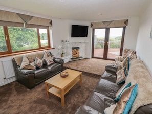 A living room with a fireplace, leather sofas, a coffee table, and a TV mounted on the wall.