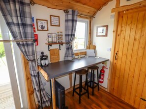 Una cocina con una mesa de madera, taburetes de bar, una cafetera y un extintor.