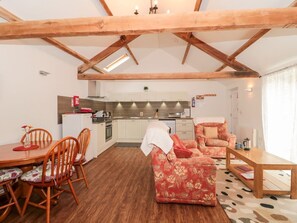 A cozy interior with a wooden ceiling, a dining area with chairs and a table, a kitchen with cabinets and appliances, and a sofa in the living area.