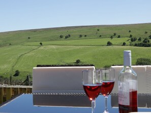 Ein Tisch mit zwei Weingläsern und einer Weinflasche, mit Blick auf einen grünen Hang.
