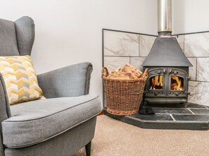 A grey sofa with a patterned cushion, a wicker basket, and a wood-burning stove. - Ash Cottage, Combe Martin (Ilfracombe)