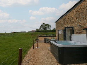 Un jacuzzi, asientos exteriores y un edificio de piedra con vistas al campo.