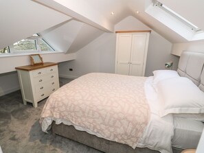 Un dormitorio con techo inclinado, una cama, un aparador y un armario.