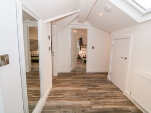 A hallway with wooden flooring, white walls, and a skylight.