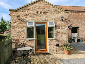 A brick house with a wooden door, a small patio with a table and chairs, and a potted plant. - Decca Cottage Nidd Grange, York (York)