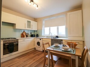 A compact kitchen with a gas stove, oven, washing machine, and a dining area with a table and chairs.