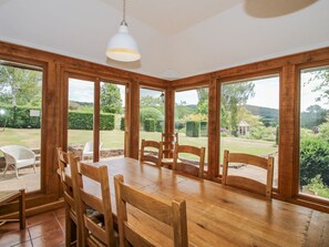 Ein Essbereich mit Holztisch und Stühlen, großen Fenstern und einer hängenden Leuchte.