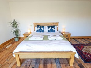 Ein hölzernes Bett mit weißer Bettwäsche, zwei Kissen mit Möwendesign, Nachttischlampen, ein Topf mit Pflanze und ein gemustertes Teppich.