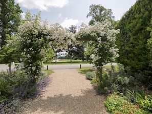 Ein Kiesweg führt zu einem weißen Blütenbogen in einem angelegten Garten.