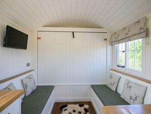 Ein Zimmer mit Sitzgelegenheit, einem an der Wand befestigten Fernseher und einem Fenster mit Vorhängen.