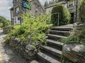 Ein Steinhaus mit einem Schild, einer Treppe, die zu einer Tür führt, und einem Heckenbewuchs davor.