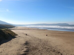 A wide sandy beach with gentle waves, a clear sky, and distant hills. - Val's Seaview, Ilfracombe (Ilfracombe)