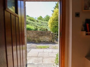 An open doorway leading to a stone wall and a garden with a wooden fence.