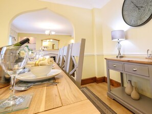 A dining area with a wooden table, chairs, a bowl of food, a wine bottle, and a clock on the wall. - Llwyn Derw, Talybont (Talybont)