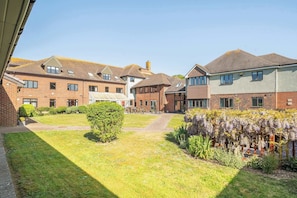 A courtyard with brick buildings, a central lawn, and flowering plants. - Marine Court First-floor Sleeps 3 (Littlehampton)