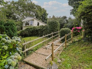 A wooden staircase leading to a house surrounded by lush greenery and flowering plants. - Vista - Stunning Views in Moelfre (Moelfre)