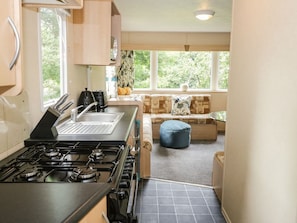 A compact kitchen with a gas stove, sink, and window overlooking a garden. - Vista - Stunning Views in Moelfre (Moelfre)