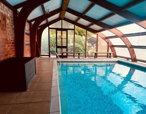 Ein Hallenbad mit freiem Blick ins Freie, einer Ziegelwand und einer überdachten Sitzgelegenheit.