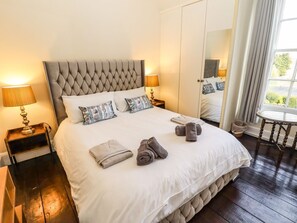 Ein Hotelzimmer mit einem großen Bett, zwei Nachttischen, einem Spiegel, einem kleinen runden Tisch und einem Fenster mit Vorhängen.