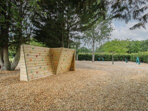 Een klimmuur met diverse grepen, omgeven door bomen en een laag mulch.