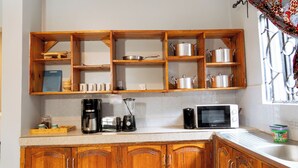A kitchen with wooden cabinets, a coffee maker, a microwave, and shelves with pots and cups. - Peaceful 2-bedroom house in charming Arusha for your getaway (Arusha)