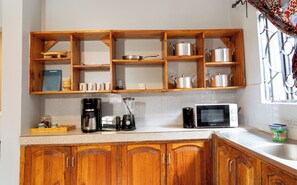 A kitchen with wooden cabinets, a coffee maker, a microwave, and shelves with pots and cups.