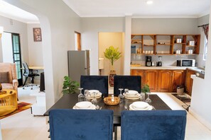 A dining area with a table set for four, a kitchen with wooden cabinets, and a living room with a sofa and a plant.