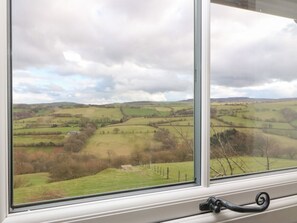 Blick aus dem Fenster auf sanfte Hügel und Felder, ein weißer Fensterrahmen und ein schwarzer Griff.