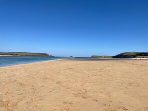 Ein weiter Sandstrand mit klarem, blauem Wasser und sanften Hügeln im Hintergrund.